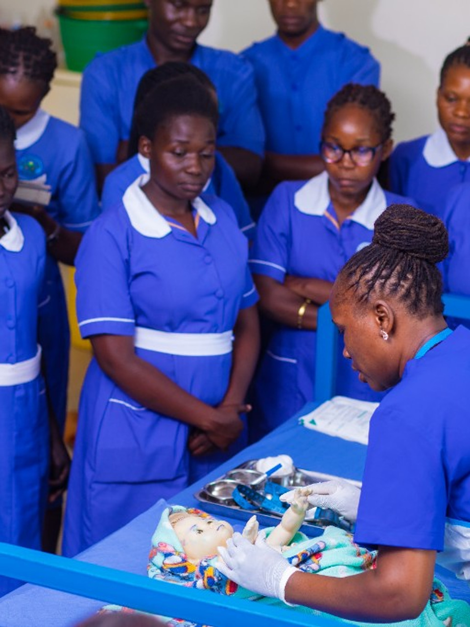Midwifery students observing infant care practice on a training mannequin
